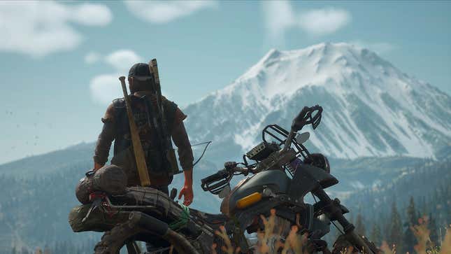Days Gone's protagonist sits with his motorcycle in front of a mountain. 